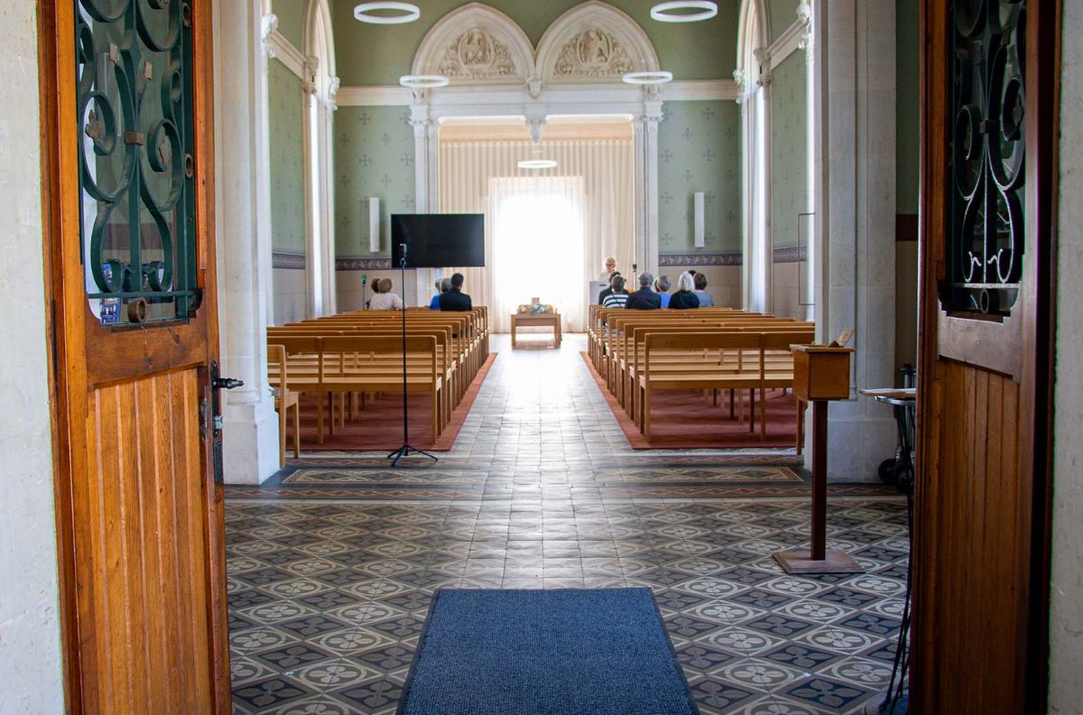 Cérémonie funéraire dans une chapelle vue par les portes ouvertes, avec écran et dispositif de diffusion
